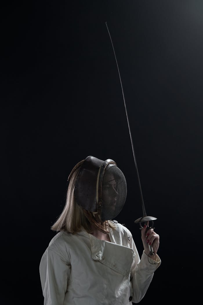Services Dramatic portrait of a female fencer holding a sword in a dark studio setting.