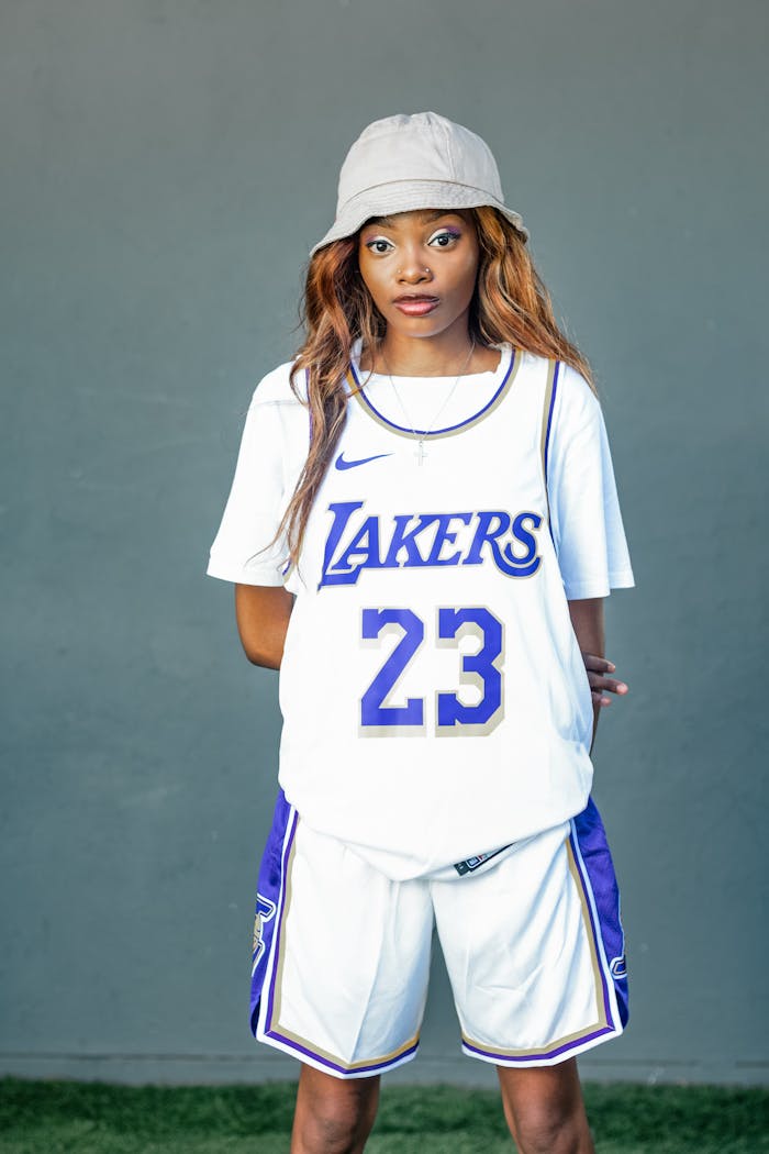 About Black woman posing in Lakers jersey and sportswear against a neutral background.