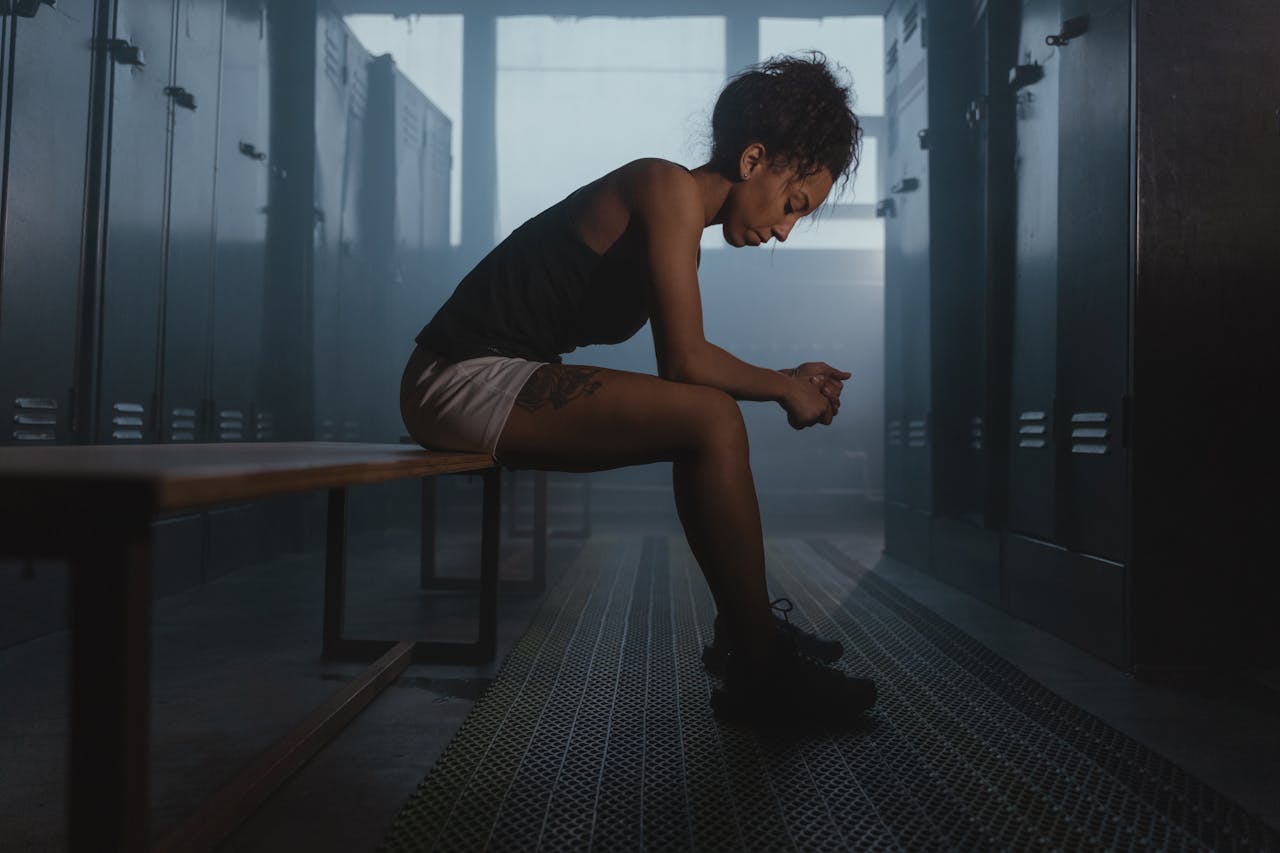 Home A contemplative athlete sits in a dimly lit locker room, embodying strength and introspection.