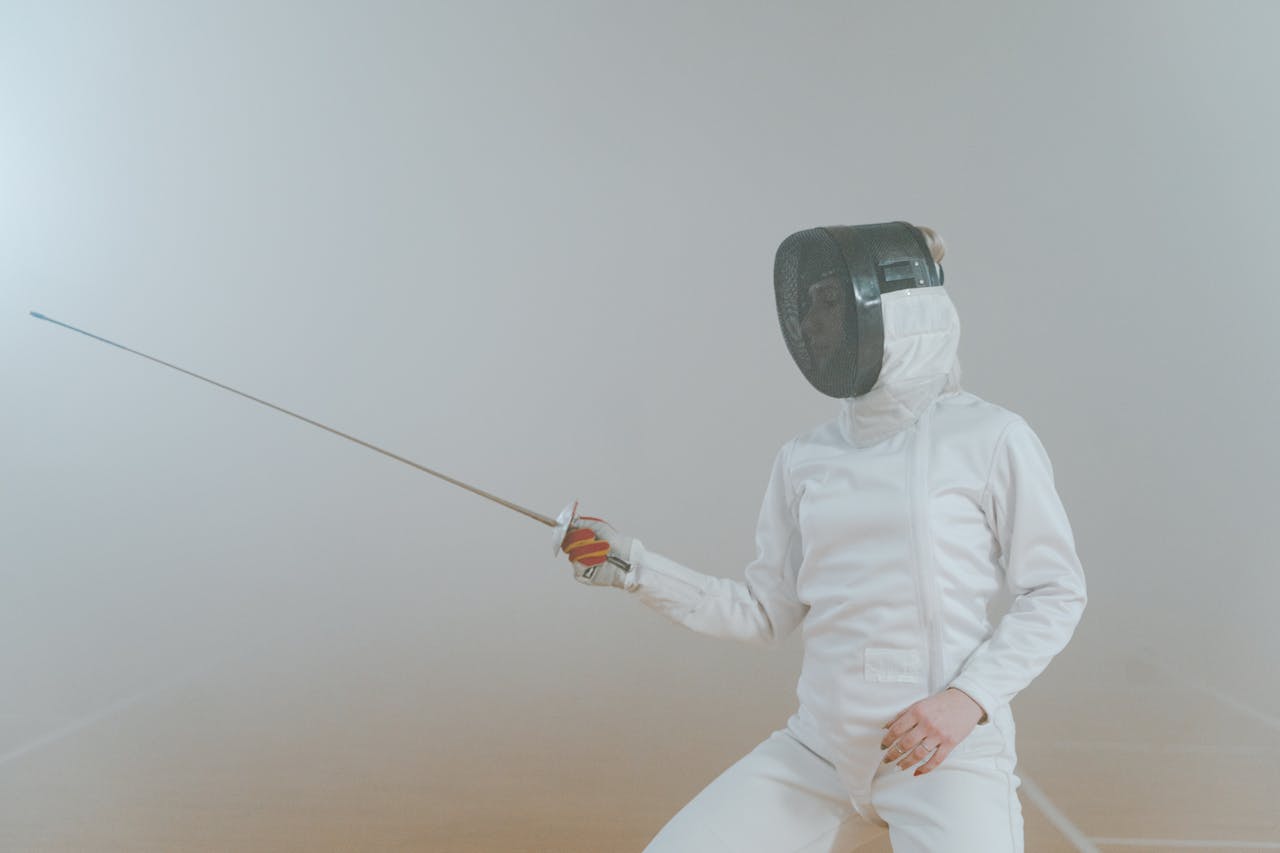 Home A female athlete in fencing gear striking an en garde pose in a foggy setting.