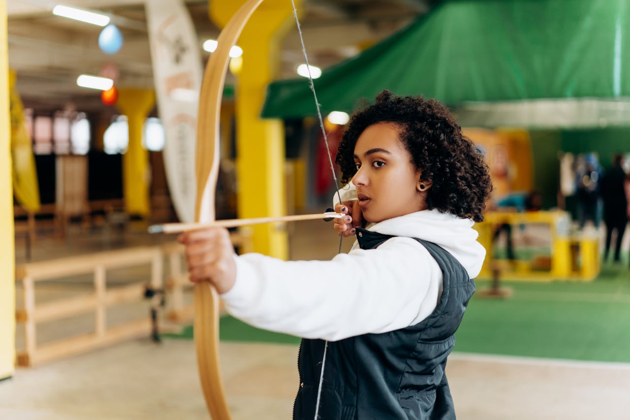 Home Young woman concentrating while practicing archery indoors. Perfecting her aim with determination.