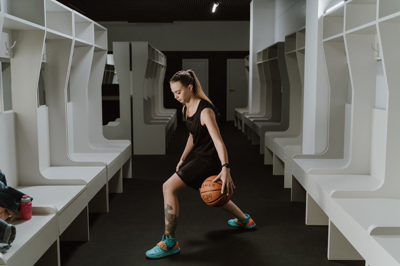 Home A female basketball player practicing dribbling in a modern indoor locker room.