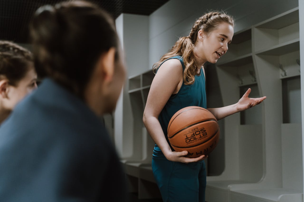 Contact A young female basketball player explains strategies to teammates in a locker room.