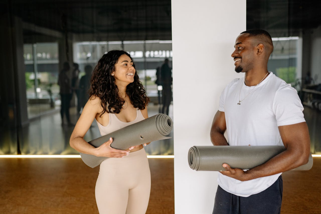 Mastering the First Impression: Your intriguing post title goes here A smiling man and woman holding yoga mats, preparing for a fitness class in a modern gym.
